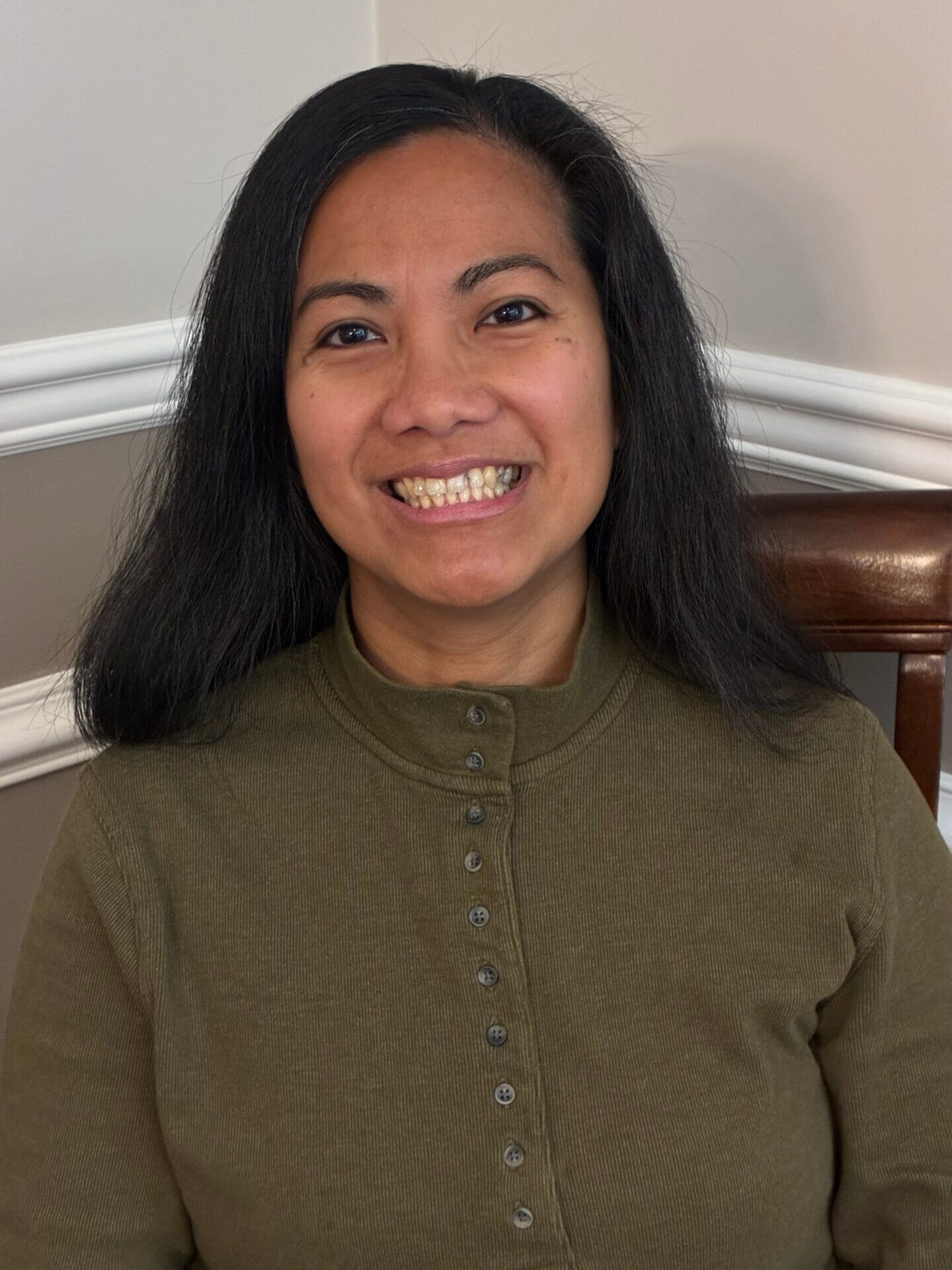 Smiling person sitting on a wooden chair.